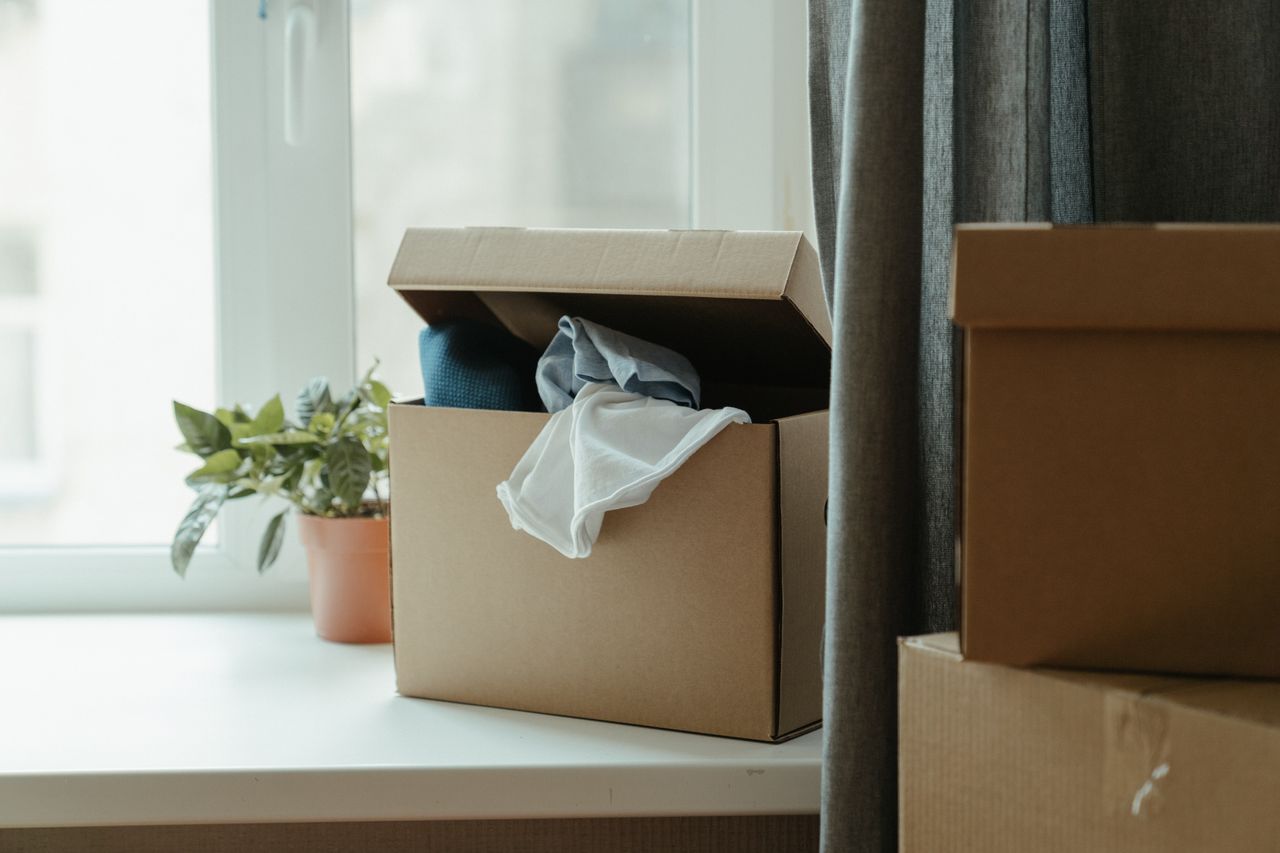 creative Open cardboard box with clothes by window, symbolizing moving or relocation.